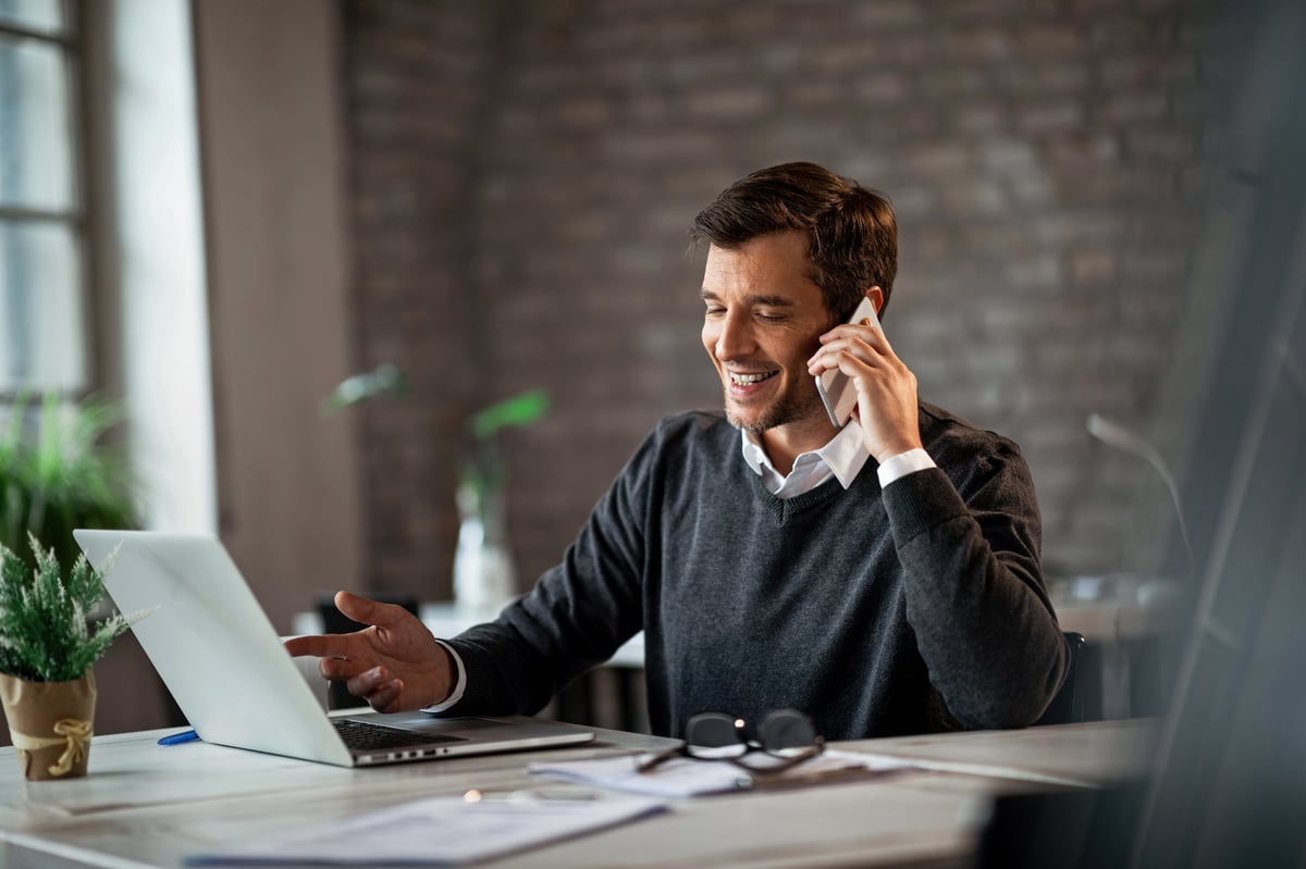Happy businessman communicating over mobile phone and working on laptop while being at work