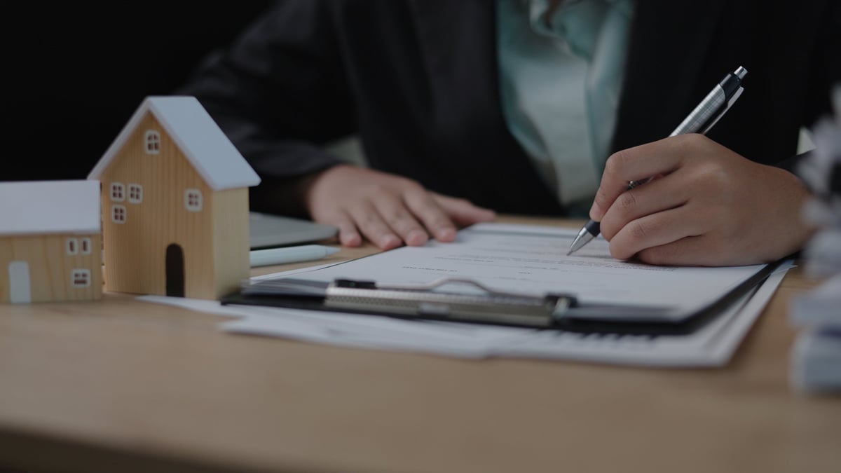 Businesswoman reviewing real estate documents with house models on office desk, mortgage, home loan, property investment, and contract concept.